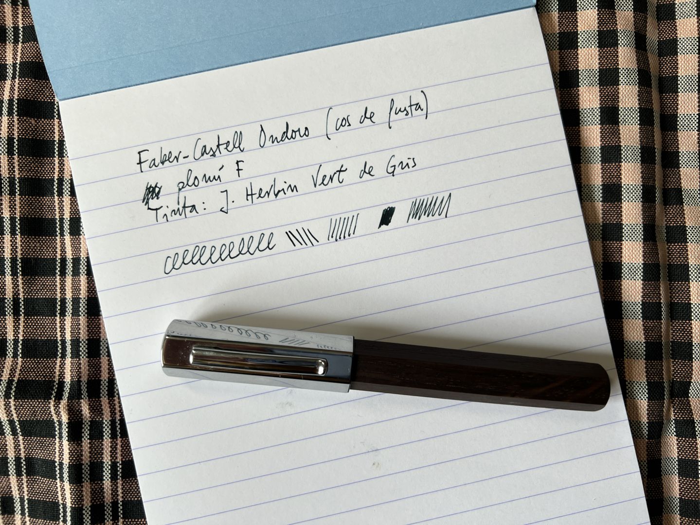 Full d’un bloc de mida A5 amb pauta. Text: Faber-Castell Ondoro, cos de fusta, plomí F, tinta J. Herbin Vert de Gris. A sota, la ploma en qüestió. Fons: un drap de roba de fer farcells.